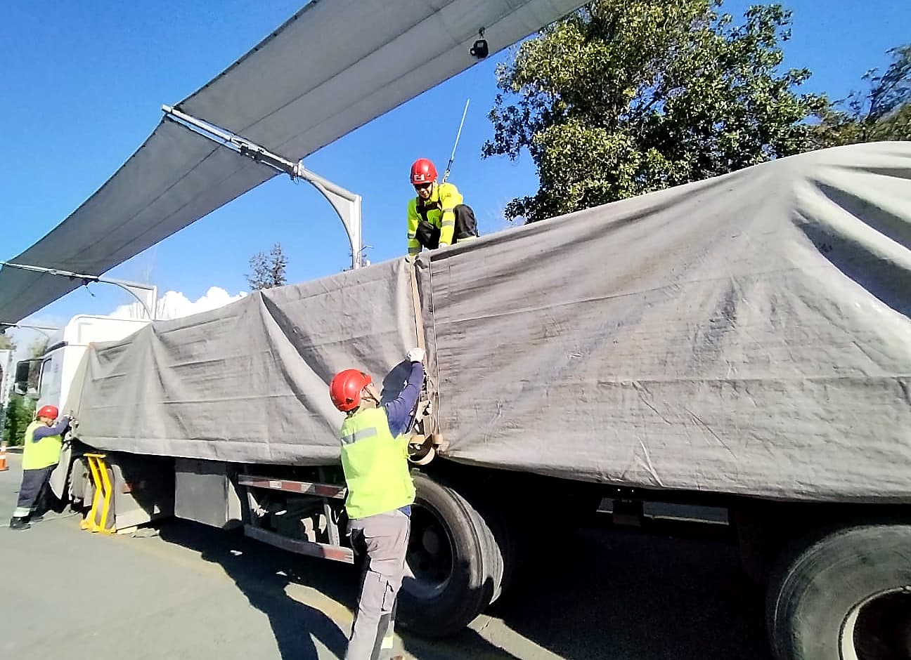 Operarios encarpando un camión en planta, con casco y chaleco reflectante